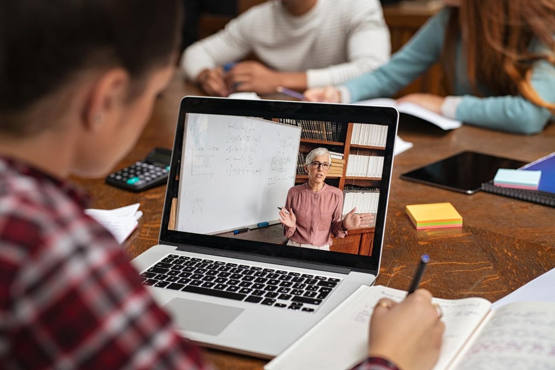 Studenter som deltar i en interaktiv distanslektion via en laptop där en lärare undervisar framför en whiteboard med matematiska ekvationer.