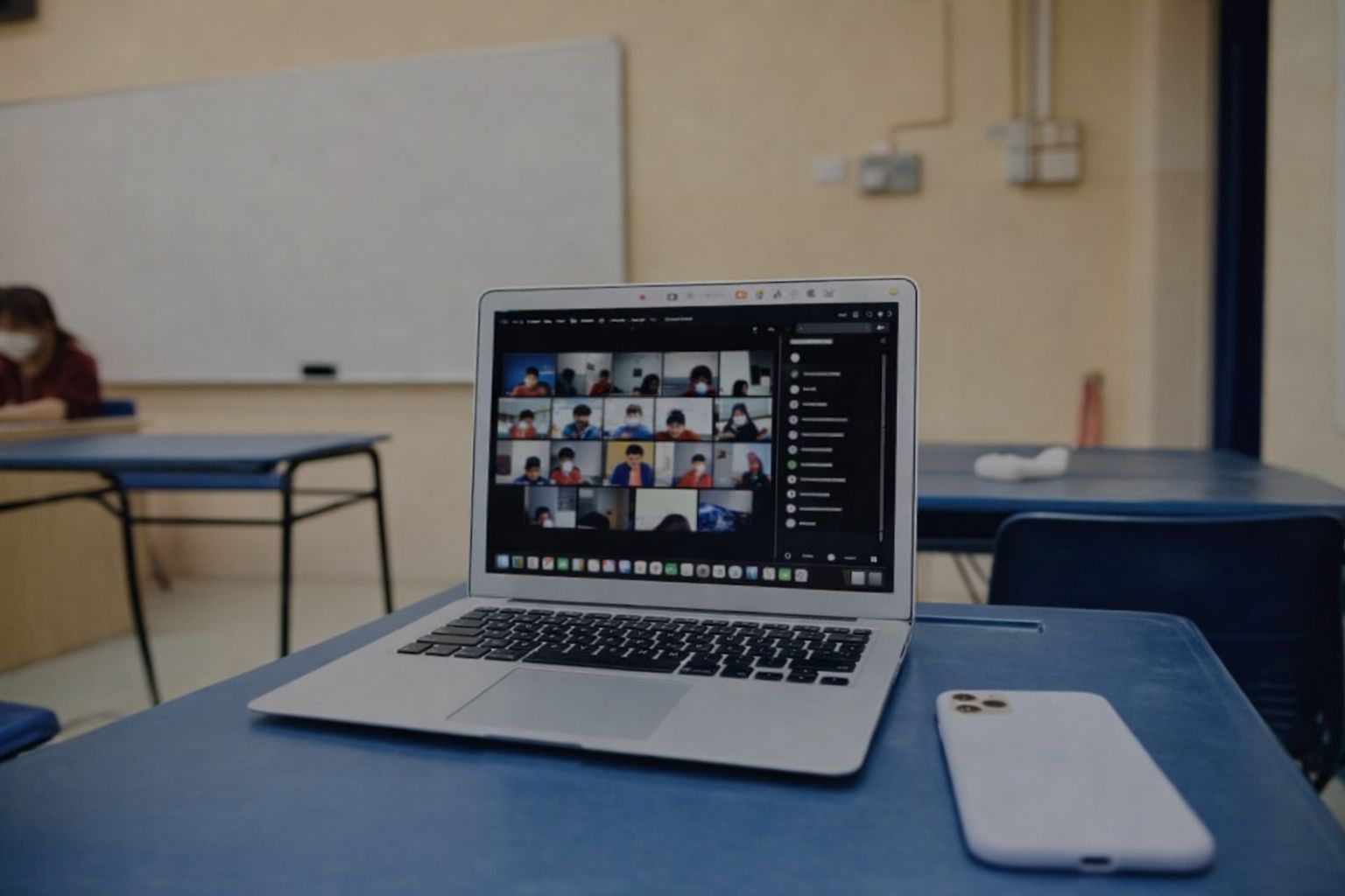 Laptop på en skolbänk visar ett digitalt videomöte med elever i ett klassrum.