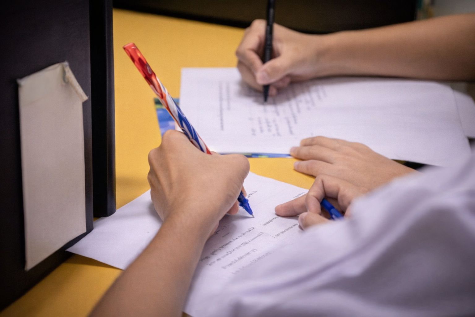 Närbild på elever som skriver på papper under en lektion i skolan.