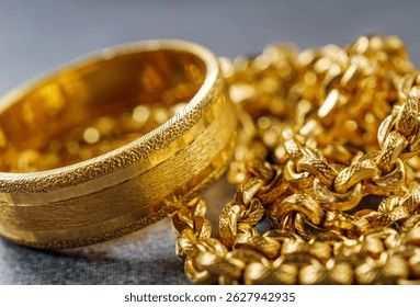 Närbild på en bred guldring och en glittrande guldkedja på en mörk bakgrund.
