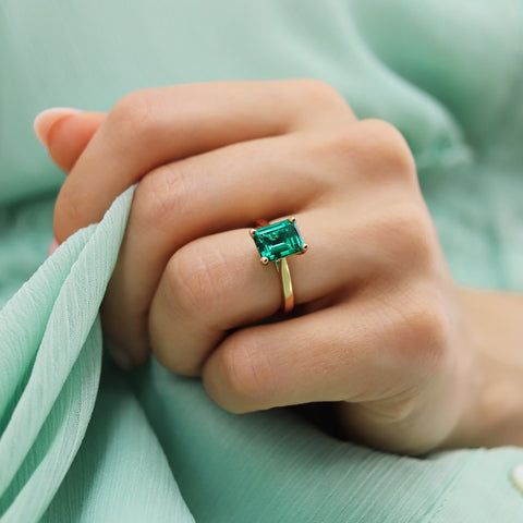 Guldring med en stor, rektangulär grön smaragd på ett finger.