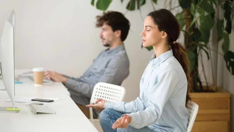 Kvinna blundar och andas lugnt vid ett skrivbord med dator
